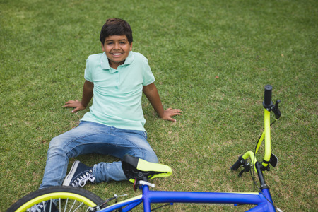Portrait of smiling boy with fallen bicycle on field at parkの写真素材