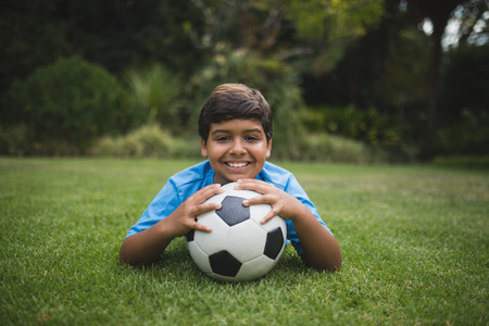 Portrait of smiling boy with soccer ball lying on field at parkの写真素材