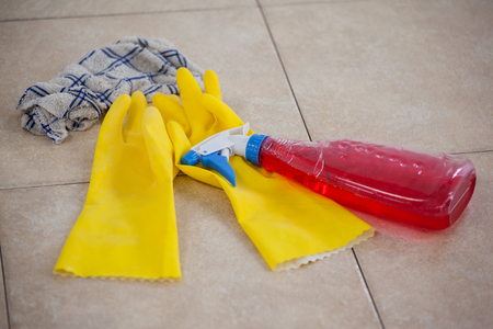 Close-up of detergent spray bottle, glove and cloth on tile floorの写真素材