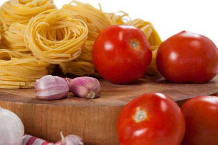 Raw fettuccine with tomatoes, garlic and onions against white backgroundの写真素材
