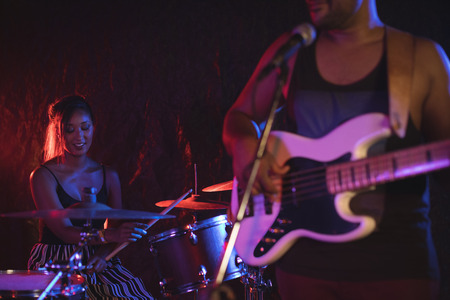 Mid section of male playing guitar with female drummer in nightclubの写真素材