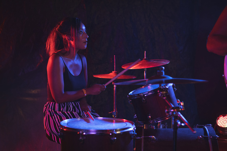 Female drummer practicing with drum kit in nightclubの写真素材
