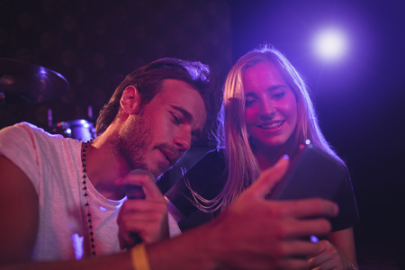 Young male and female musicians using mobile phone while practicing in nightclubの写真素材