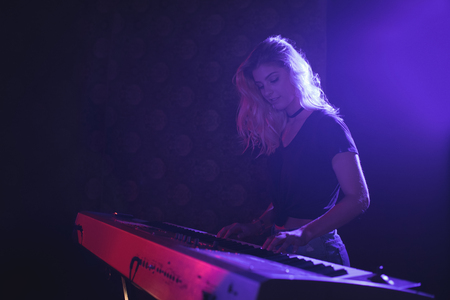 Young female musician playing piano on illuminated stage in nightclubの写真素材