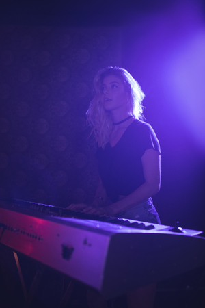 Beautiful young woman playing piano on illuminated stage in nightclubの写真素材
