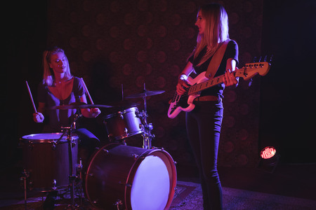 Confident female drummer and guitarist performing on illuminated stage in nightclubの写真素材