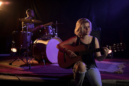 Female practicing guitar while sitting on stage in nightclubの写真素材