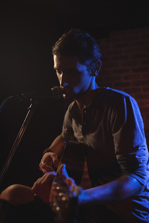 Confident male singer playing guitar while performing in nightclubの写真素材