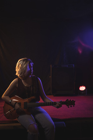 Confident female guitarist playing guitar while sitting on stage in nightclubの写真素材