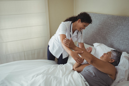 Female doctor comforting senior woman on bed at homeの写真素材