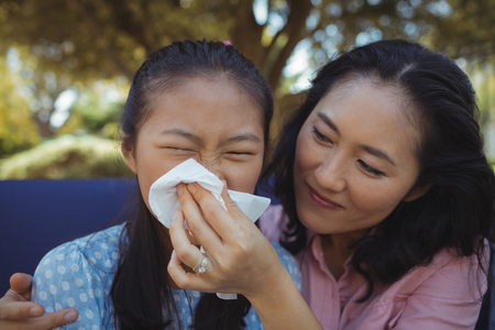 Mother helping daughter blow her nose at homeの写真素材