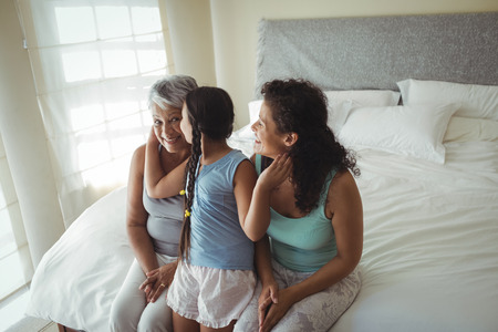 Daughter kissing grandmother on cheeks in bed room at home