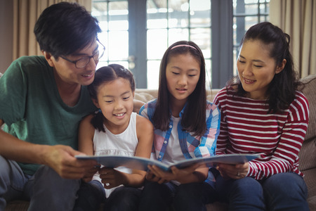 Family watching photo album together in living room at home