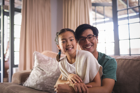Portrait of smiling father and daughter relaxing on sofa in living room at homeの写真素材