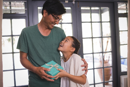 Daughter giving gift box to father in living room at homeの写真素材