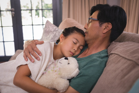 Father and daughter relaxing on sofa in living room at homeの写真素材