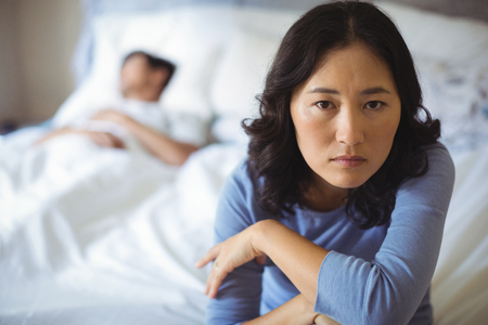 Upset woman sitting on bed in bedroom at homeの写真素材