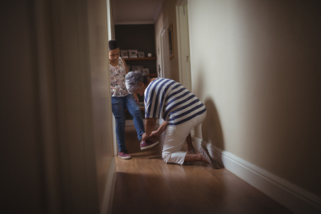 Grandmother helping granddaughter to wear shoes at homeの写真素材