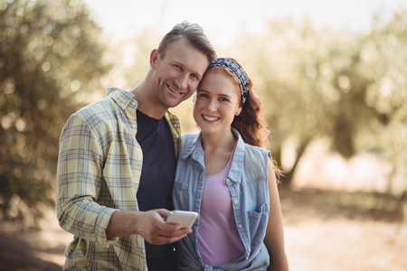 Portrait of smiling young couple with mobile phone at olive farmの写真素材