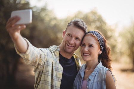 Cheerful young couple taking selfie at olive farm on sunny day