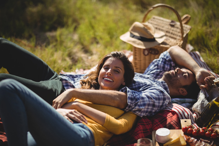Smiling young woman with boyfriend relaxing on picnic blanket at olive farm during sunny dayの写真素材