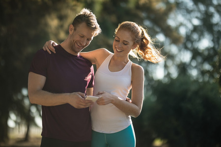Low angle view of happy young couple using mobile phone on sunny dayの写真素材