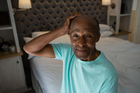 Portrait of smiling senior man sitting on bed at homeの写真素材