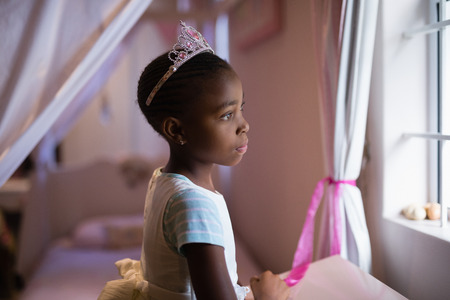 Side view of thoughtful girl wearing crown standing in bedroom at homeの写真素材