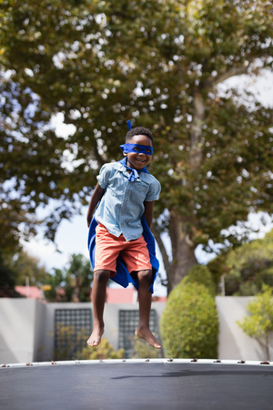 Full length of boy in superhero costume jumping on trampolineの写真素材