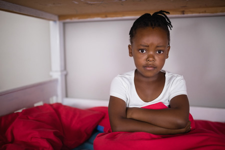 Portrait of upset little girl sitting on bed at homeの写真素材