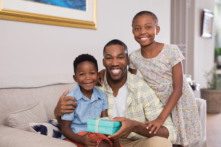 Portrait of smiling father and children holding gift box on sofa at home