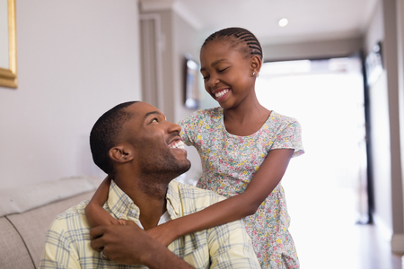 Smiling father and daughter sitting on sofa in living room at homeの写真素材