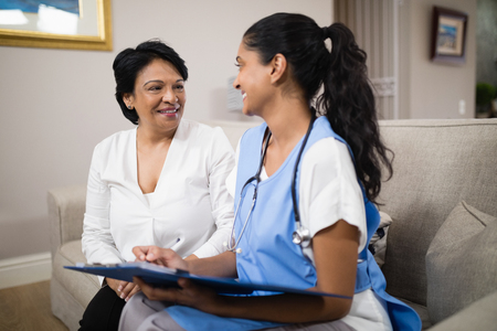 Smiling doctor with female patient sitting on sofa at homeの写真素材