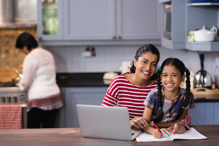 Portrait of smiling girl with mother studying in kitchen at homeの写真素材