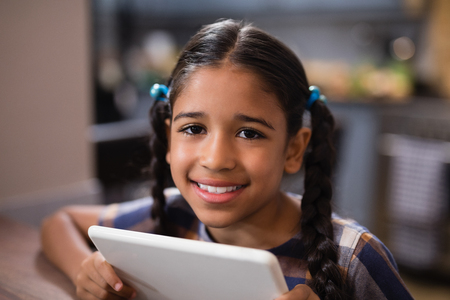 Portrait of smiling girl holding digital tablet in kitchen at homeの写真素材