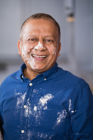 Portrait of happy mature man with flour on face and shirt at homeの写真素材