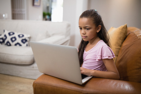 Girl using laptop while sitting on sofa at homeの写真素材