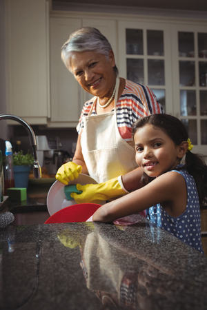 Portrait of grandmother and granddaughter washing utensil in kitchen sink at homeの写真素材