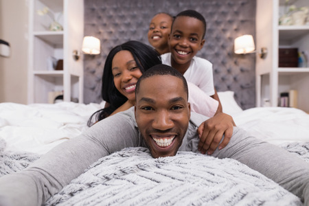 Portrait of happy man lying with family on bed at homeの写真素材