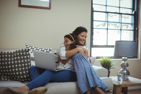 Mother hugging daughter in living room at homeの写真素材