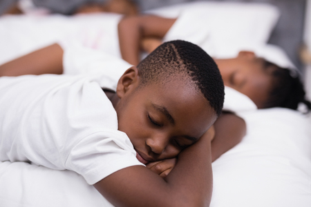 Boy sleeping on bed with sister in background at homeの写真素材