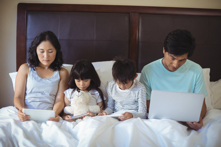 Family using digital tablet, mobile phone and laptop on bed in the bed room at homeの写真素材