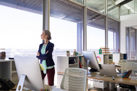 Female executive standing with arms crossed and looking at window in office