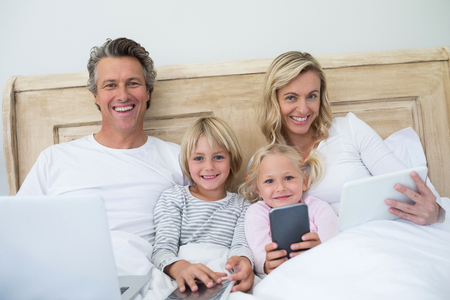 Family using digital tablet, mobile phone and laptop on bed in the bed room at homeの写真素材