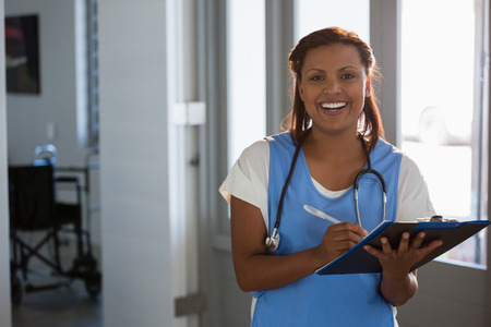 Smiling doctor writing on clipboard in the hospitalの写真素材