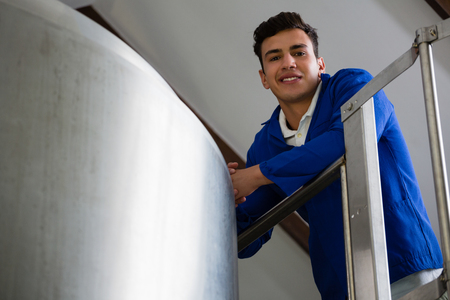 Low angle portrait of male worker standing by storage tank at brewery