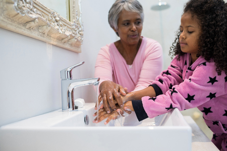 Grandmother and granddaughter washing hands in bathroom sink at homeの写真素材