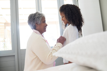 Grandmother dressing up her granddaughter in bedroom at homeの写真素材