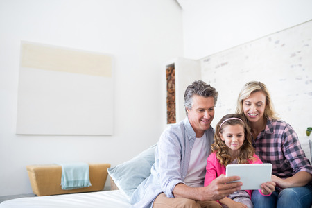Smiling family using digital tablet together in living room at homeの写真素材