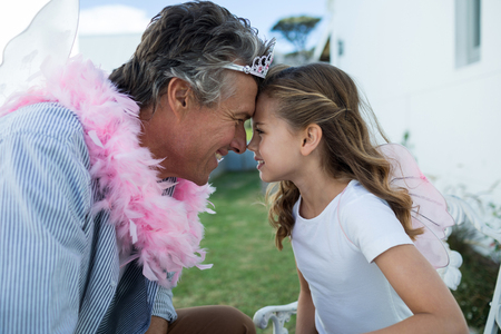 Smiling father and daughter in fairy costume standing face to face in gardenの写真素材